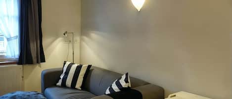 A living room with a sofa, a lamp, a table, and a window with curtains.