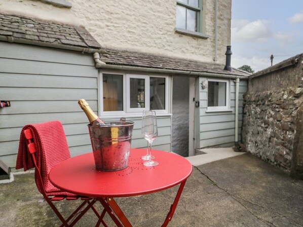 A red metal table with a bucket containing a bottle and a glass, set against a building with a stone wall and a window.