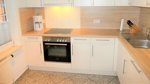 A compact kitchen with white cabinets, a built-in oven, a coffee maker, and a sink. - Lüttje Fischerhuus - Holiday home Lüttje Fischerhuus: 400 m to the beach, terrace & (Wyk auf Föhr)