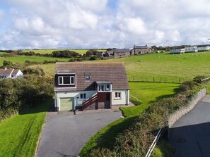 A two-story house with a garage, surrounded by a green field and a stone wall.