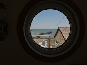A round window with a view of a rocky shoreline and calm sea. - Min Y Traeth, Bull Bay (Amlwch)