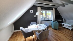 Un comedor con una mesa redonda, sillas, una lámpara colgante y vistas al exterior a través de una ventana.
