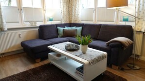 Ett vardagsrum med en soffa i mörk färg, ett vitt soffbord, en golvlampa och ett element.