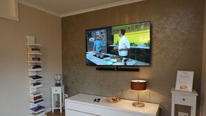Ett vardagsrum med en platt-TV som är monterad på väggen, ett vitt konsolbord, en lampa, en bokhylla och ett litet sidobord.