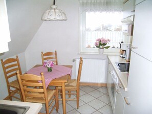 Uma cozinha pequena com uma mesa de jantar, cadeiras, uma janela florida e um radiador.