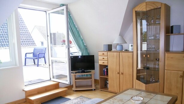 A living room with a TV, wooden cabinet, and a window with curtains. - Jordan - FW OG - Allergy-friendly vacation apartment with balcony in Wyk on Föhr, (Wyk auf Föhr)