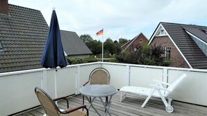 A balcony with a table and chairs, a flag, and a view of neighboring houses. - Jordan - FW OG - Allergy-friendly vacation apartment with balcony in Wyk on Föhr, (Wyk auf Föhr)