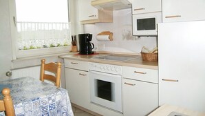 A compact kitchen with white cabinets, a microwave, an oven, a sink, and a window with lace curtains. - Jordan - FW OG - Allergy-friendly vacation apartment with balcony in Wyk on Föhr, (Wyk auf Föhr)