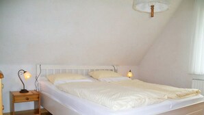 A single bed with white bedding in a room with wooden flooring and white walls. - Jordan - FW OG - Allergy-friendly vacation apartment with balcony in Wyk on Föhr, (Wyk auf Föhr)