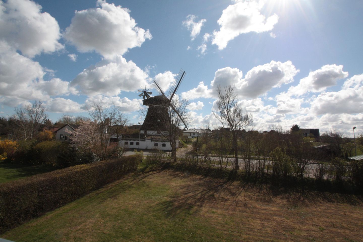 A windmill, a white building, and a grassy area with trees.
