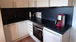 Una cuina compacta amb armaris blancs, un taulell negre, una cafetera i un forn.