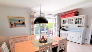 Ein Essbereich mit einem Holztisch, weißen Stühlen, einer schwarzen Pendelleuchte und einem Schrank mit roten Ordnern.