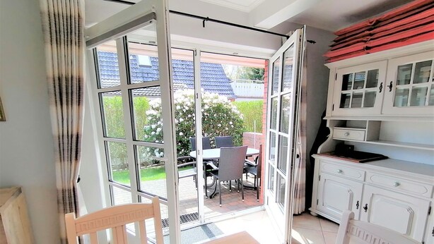 Ein Zimmer mit Esstisch, Stühlen, einem weißen Schrank und einer Glastür zum Balkon mit Tisch und Stühlen.