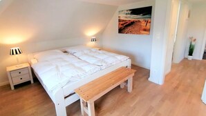 Ein Schlafzimmer mit einem weißen Bett, zwei Nachttischlampen, einer hölzernen Bank und einem Gemälde an der Wand.
