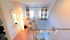 Eine Treppe mit Metallgeländer, ein Korbstuhl und ein Fenster mit Vorhängen.
