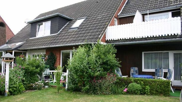 Ett tvåvåningshus med ett sluttande tak, en inhägnad trädgård och ett garage som syns.