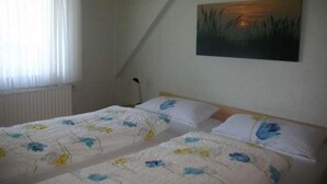 Ett rum med två sängar, ett element, ett fönster med gardiner och en tavla på väggen.