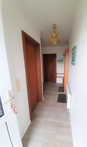 A hallway with wooden doors, a light fixture, a painting, and a framed picture on the wall. - Strandläufer, Whg. 7 - Apartment Strandläufer Whg. 7 - close to the beach in Wyk (Wyk auf Föhr)