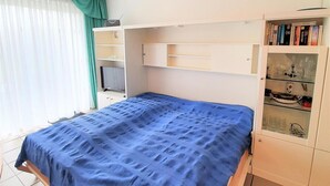 Ein Schlafzimmer mit einem Bett, einem Schreibtisch und einer Kommode mit Büchern und Dekorationsgegenständen.