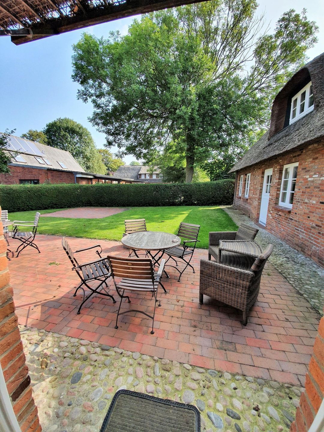 A patio area with outdoor furniture, a brick floor, and a hedge.