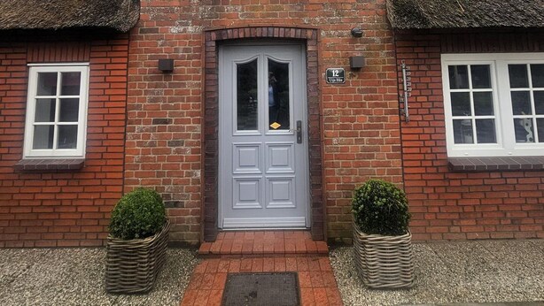 A two-story brick house with a grey door, a small window above the door, and a thatched roof. - Uijs Hüs - Allergy-friendly vacation home Uijs Hüs with garden & terrace in (Borgsum)
