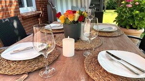 A wooden dining table set with plates, cutlery, and wine glasses, surrounded by woven placemats and a candle. - Uijs Hüs - Allergy-friendly vacation home Uijs Hüs with garden & terrace in (Borgsum)