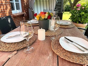 Ein Holztisch ist gedeckt mit Tellern, Besteck und Weingläsern, umgeben von gewebten Tischsets und einer Kerze.