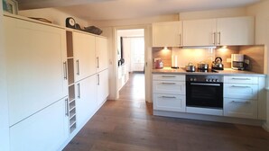 A modern kitchen with white cabinetry, a built-in oven, and a coffee maker. - Uijs Hüs - Allergy-friendly vacation home Uijs Hüs with garden & terrace in (Borgsum)