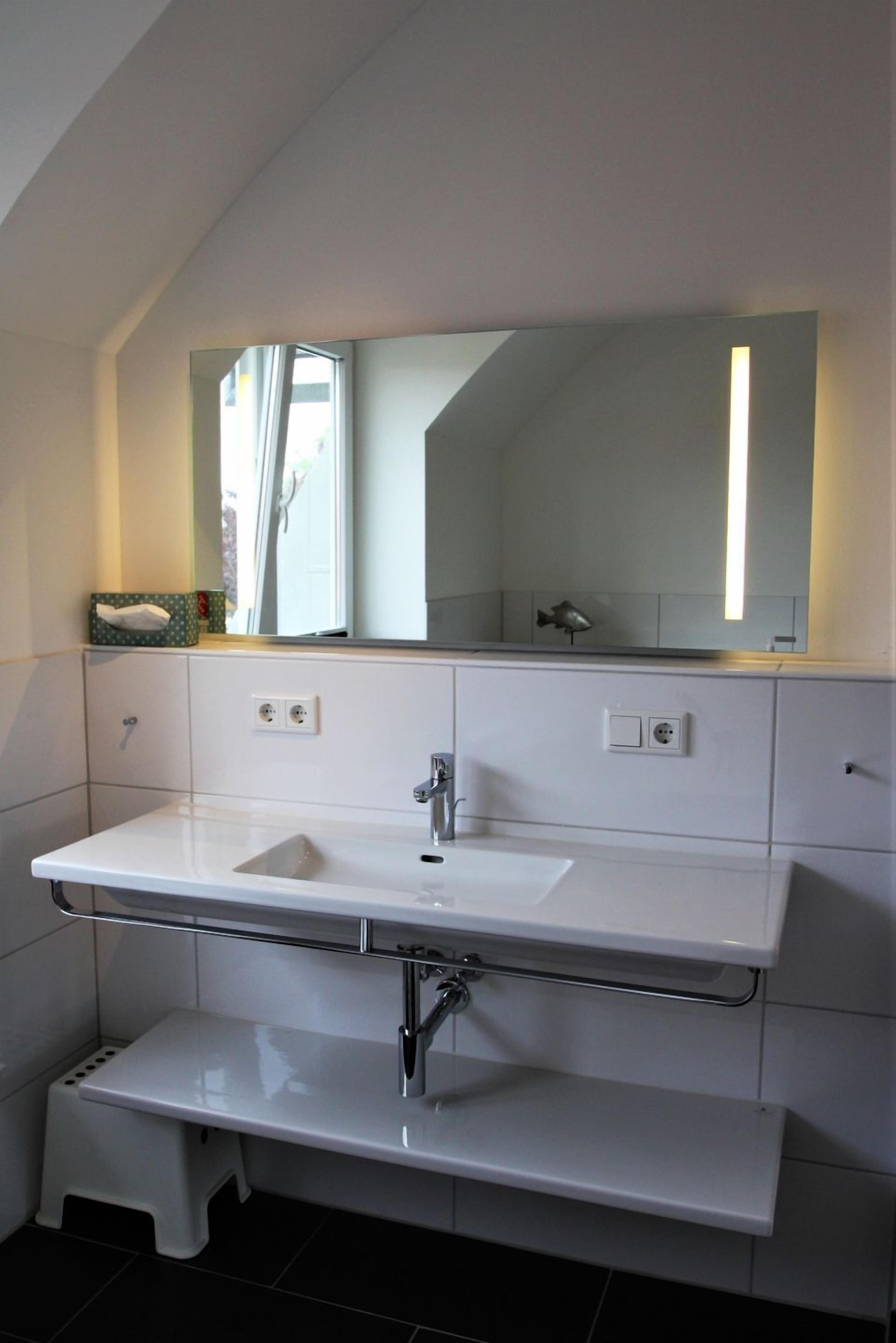 Une salle de bain moderne avec un meuble-lavabo blanc, un grand miroir et un petit tabouret.