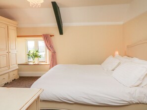 Un dormitorio con cama, cómoda, ventana con cortinas y candelabro.