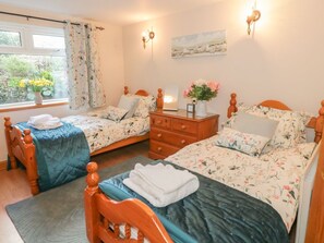A bedroom with two wooden beds, a dresser, a nightstand, and a window with curtains. - Ysgubor Newydd, Conwy (Conwy)
