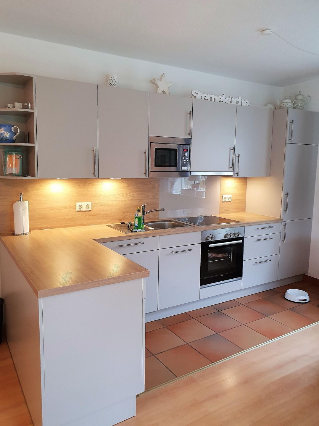 Eine moderne Küche mit weißen Schränken, einer Mikrowelle, einem Backofen und einem Spülbecken.