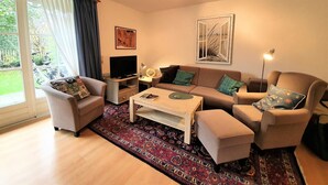 Una sala de estar con sofá, sillones, una mesa de centro, televisor y una alfombra estampada.