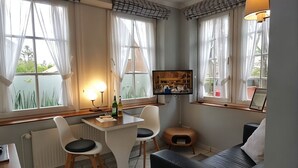 Een kamer met een eettafel, twee stoelen, een bank, een televisie en een raam met gordijnen.