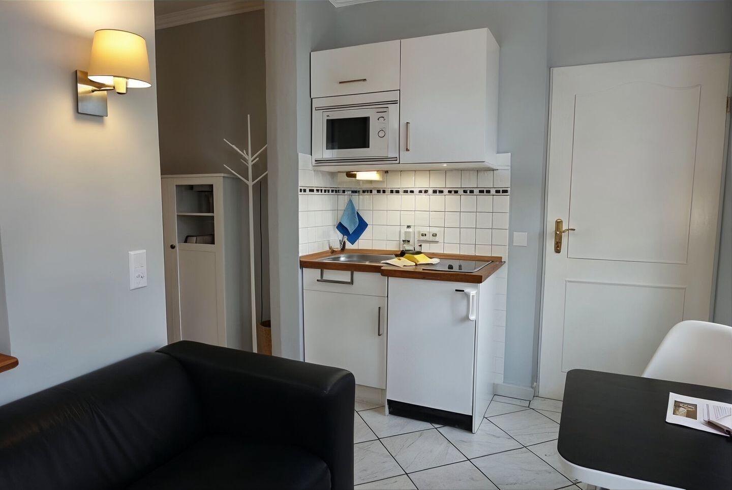 Eine kompakte Küche mit Mikrowelle, Herd und weißen Schränken. Ein schwarzes Sofa und ein kleiner Tisch mit einer Speisekarte sind ebenfalls vorhanden.
