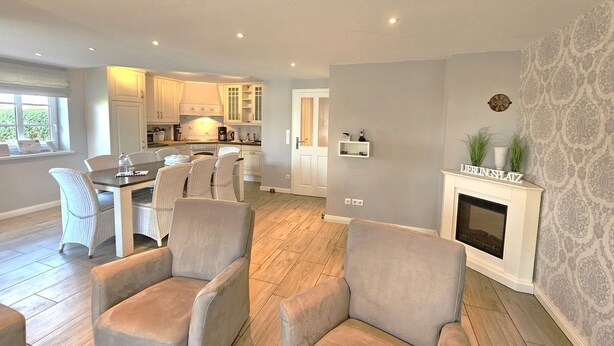 A spacious living room with a fireplace, a dining area with a table and chairs, and a kitchen in the background. - Golfoase 1 - Semi-detached house for 6 people - Golfoase 1: Semi-detached house for 6 people (Oevenum)