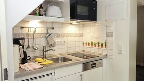 Kompakti keittiö, jossa on valkoiset kaapit, sisäänrakennettu mikroaaltouuni, ruostumattomasta teräksestä valmistettu pesuallas ja astiateline.