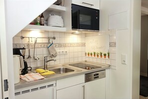 Eine kleine Küche mit weißen Schränken, einer eingebauten Mikrowelle, einer Edelstahl-Spüle und einem Geschirrgestell.