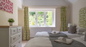 A hotel room with two beds, a window with curtains, a dresser, and a plant. - Hazelseat House, Ulverston (Ulverston)