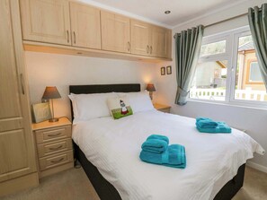 A hotel room with a bed, two bedside lamps, a nightstand, a window with curtains, and wooden cabinets.