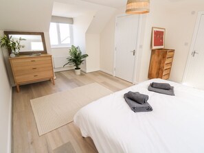Een slaapkamer met een bed, een kaptafel, een spiegel, een kamerplant en een raam.