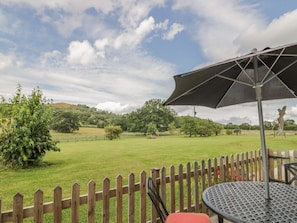 A patio with a table and chairs, a wooden fence, and a view of a grassy field and trees. - The Farmhouse, Ledsham (Ledbury)