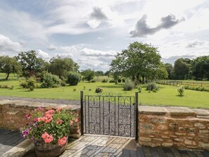 A stone wall with a metal gate leading to a grassy area with trees. - The Farmhouse, Ledsham (Ledbury)