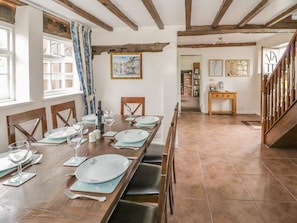 A dining area with a long wooden table set for a meal, a staircase, and a view of the outside. - The Farmhouse, Ledsham (Ledbury)