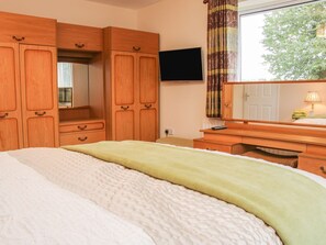 Ein Schlafzimmer mit Bett, Holzschrank, Fernseher und einem Fenster mit Vorhängen.