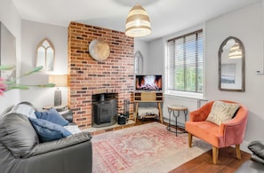 Una sala de estar con chimenea de ladrillo, televisor, sofá, sillón y ventana con persianas.