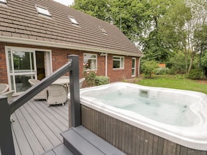 A house with a hot tub on a wooden deck, a brick exterior, and a glass door leading to a patio area.