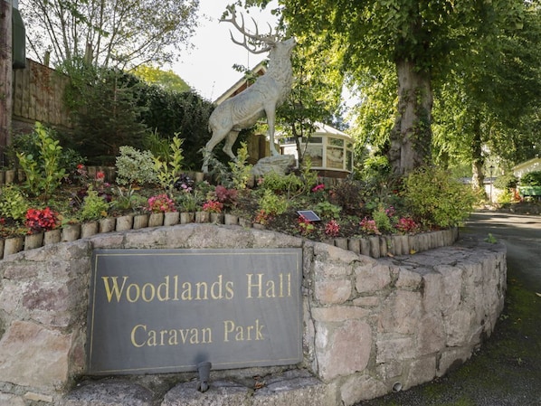 Eine Steinsäule mit einem Schild für den Woodlands Hall Caravan Park, umgeben von einem Garten mit verschiedenen Pflanzen und einer Steinstatue eines Wolfes.