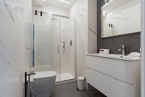 Ein modernes Badezimmer mit einer begehbaren Glasdusche, Toilette, Waschbecken und Spiegel.