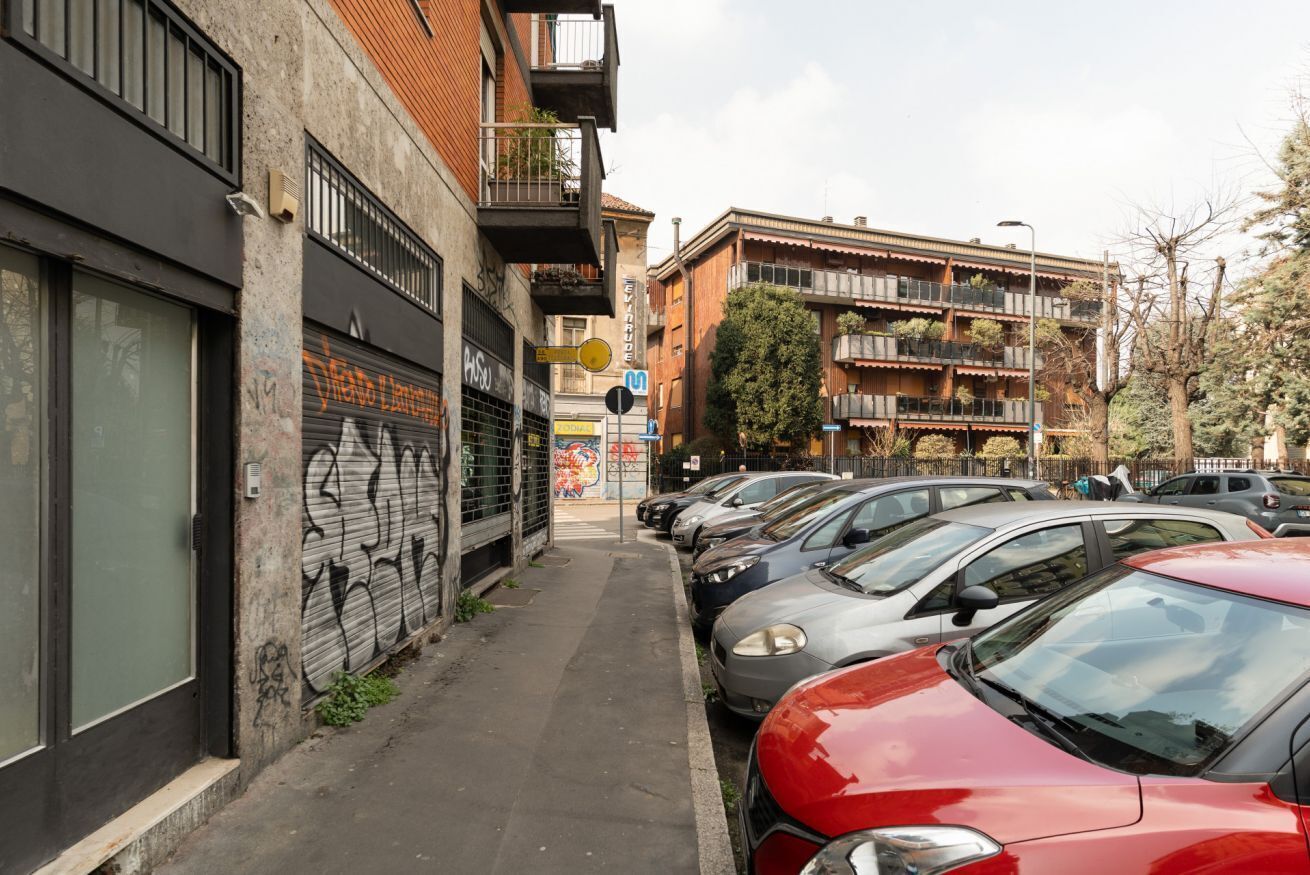 A narrow street lined with parked cars and buildings with balconies.